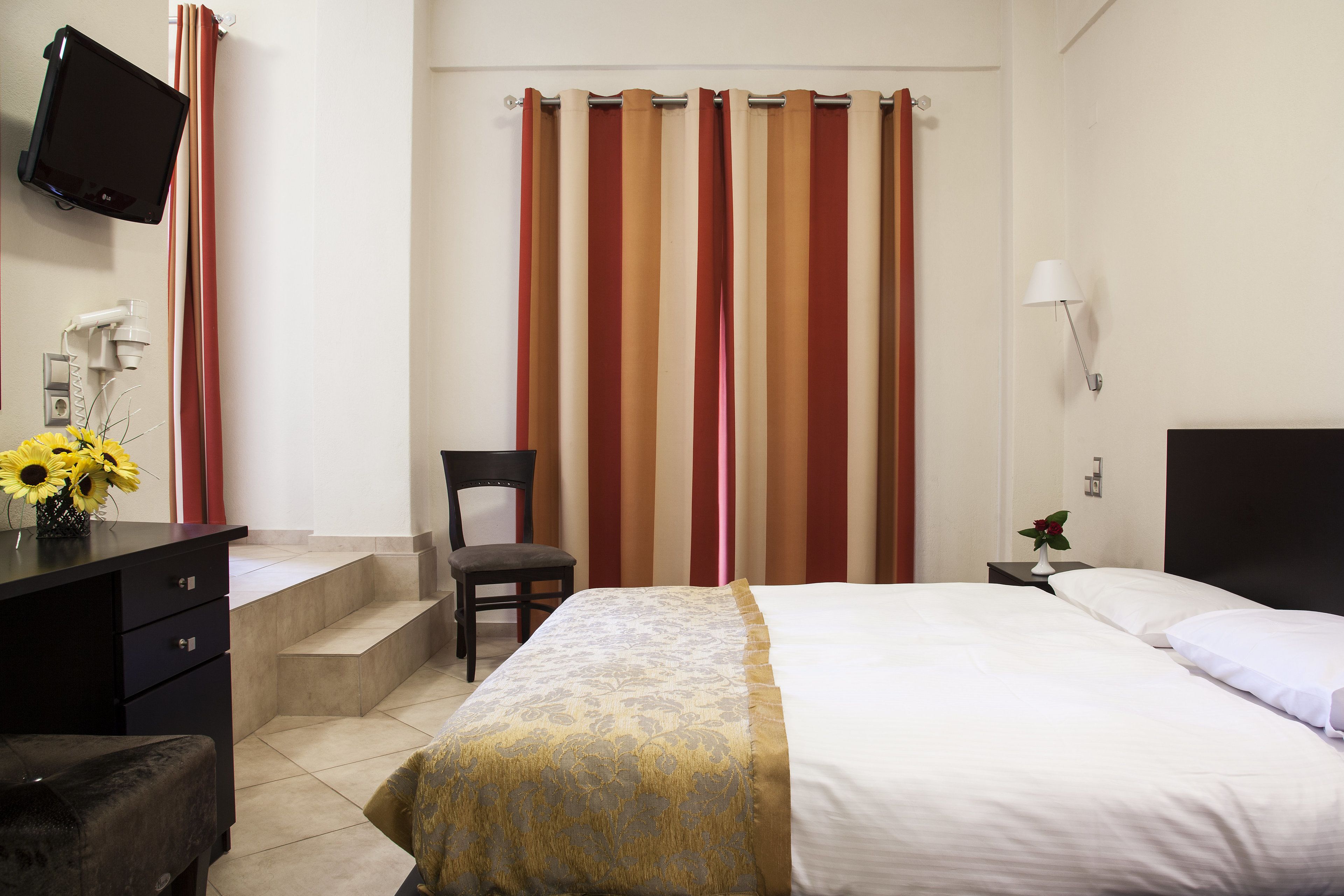 Een hotelkamer met een bed, een bureau met een computer, een stoel en een aan de muur bevestigde televisie.