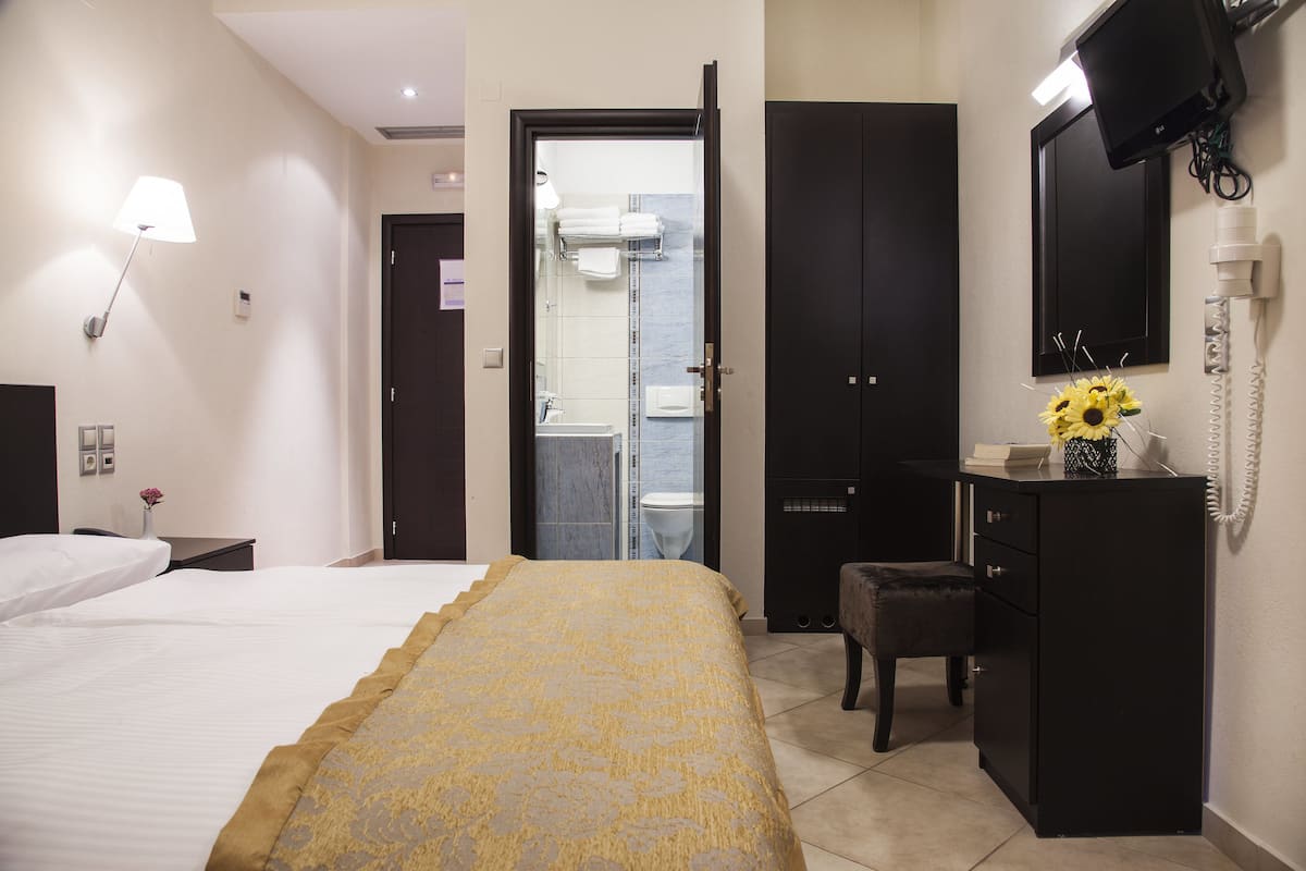 A hotel room with a bed, a desk, a chair, a wardrobe, and a bathroom visible through an open door.