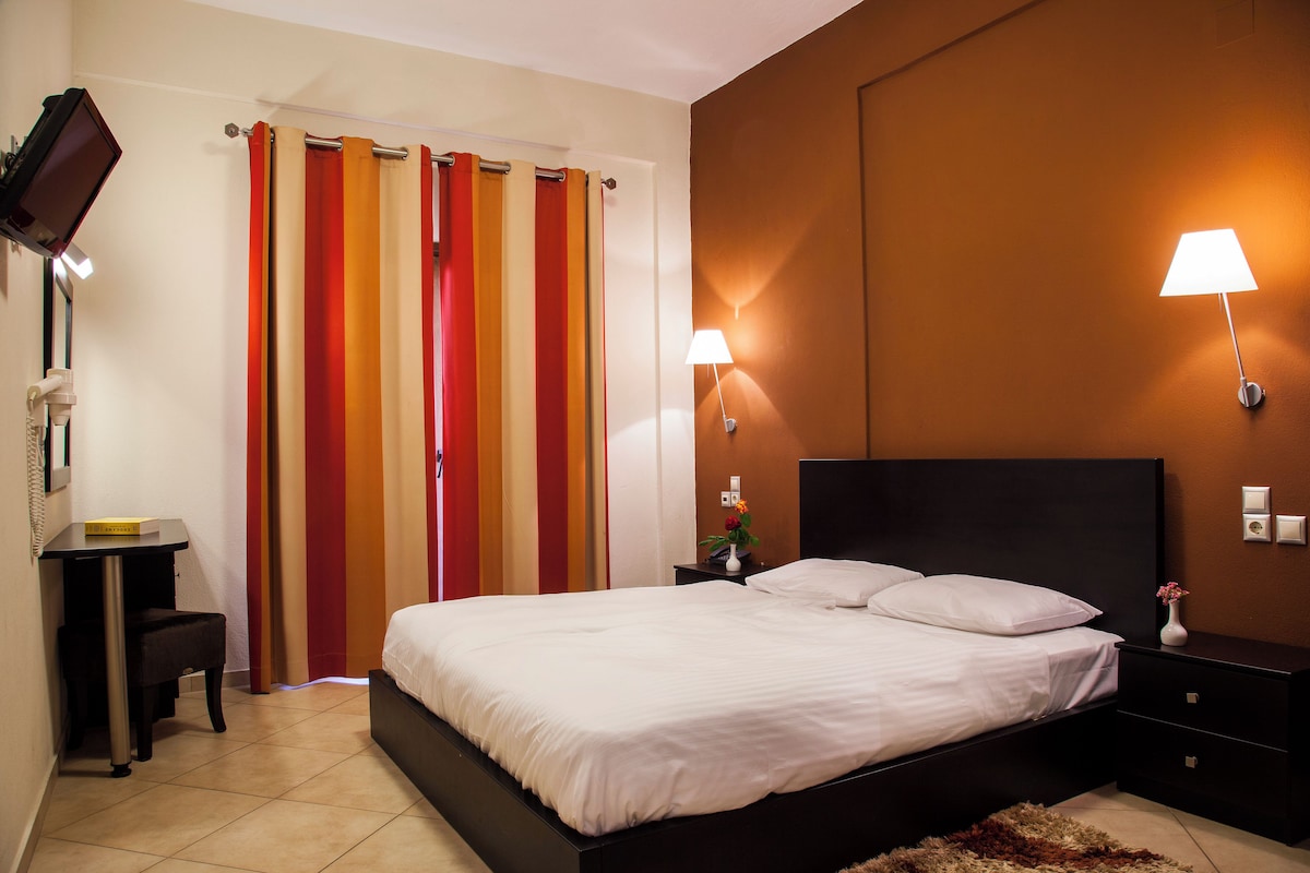 Quarto com cama, mesas de cabeceira, escrivaninha e uma cadeira.