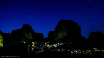 Vista nocturna de un pueblo situado entre grandes formaciones rocosas, con edificios y farolas a la vista.