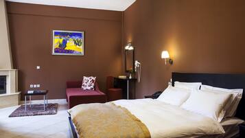 A hotel room with a bed, a desk, a chair, a painting on the wall, and a nightstand with a lamp.