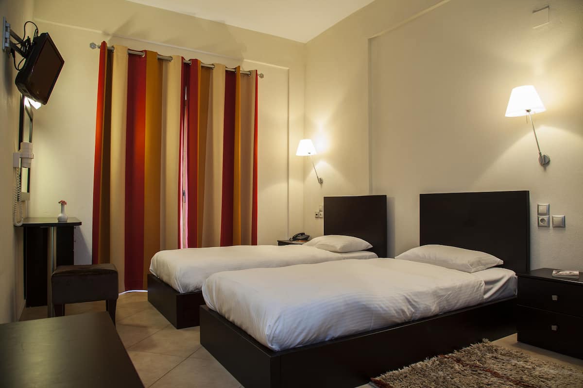 A hotel room with two beds, a desk, a chair, a lamp, and a curtain.