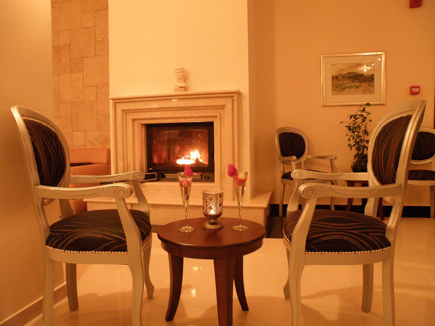 Una habitación acogedora con chimenea, dos sillones tapizados, una mesita con una vela y un cuadro enmarcado en la pared.