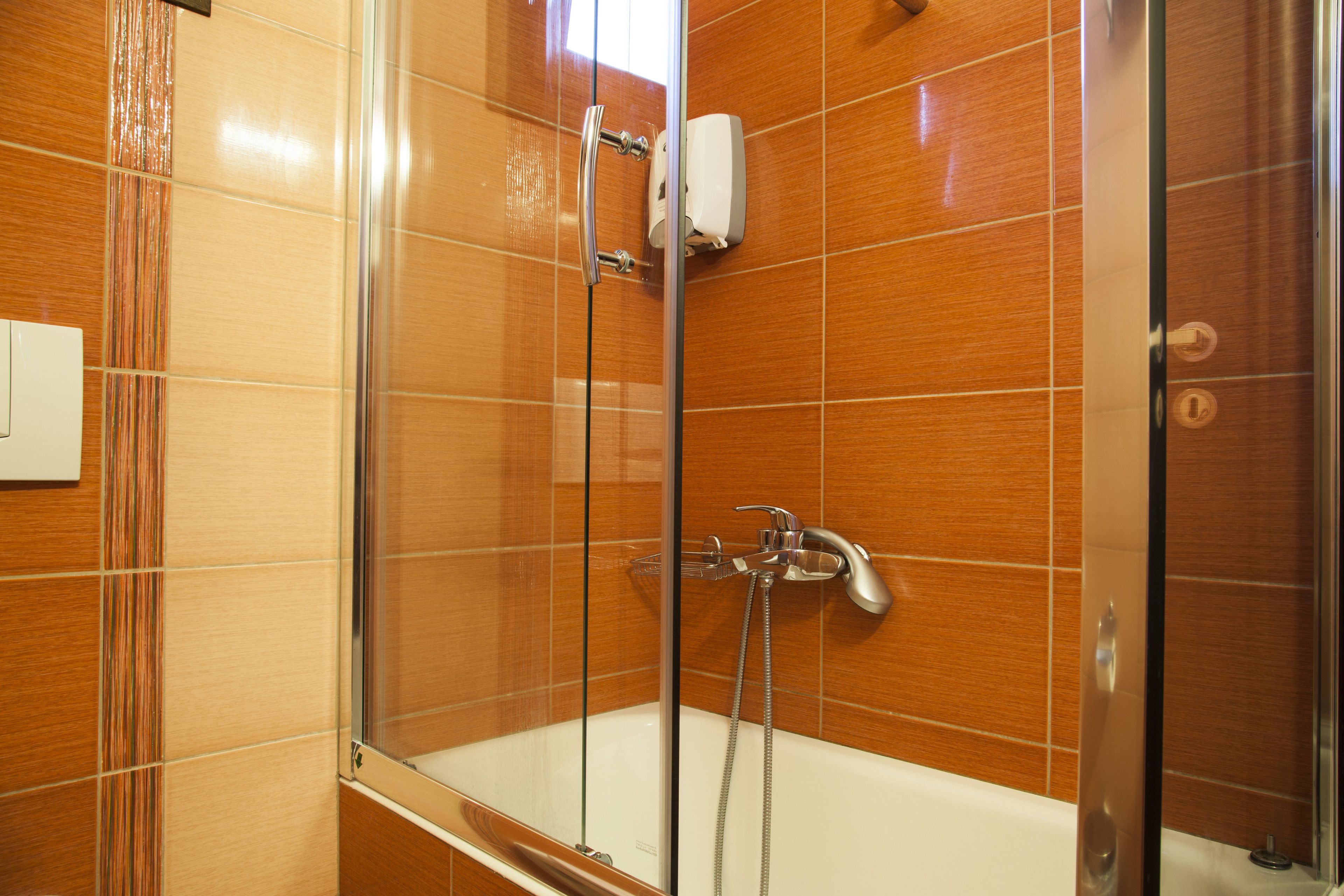 Eine Dusche mit Glastür, einer Handbrause und einem am Wand montierten Wasserhahn.