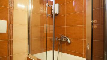 Eine Dusche mit Glastür, einer Handbrause und einem am Wand montierten Wasserhahn.