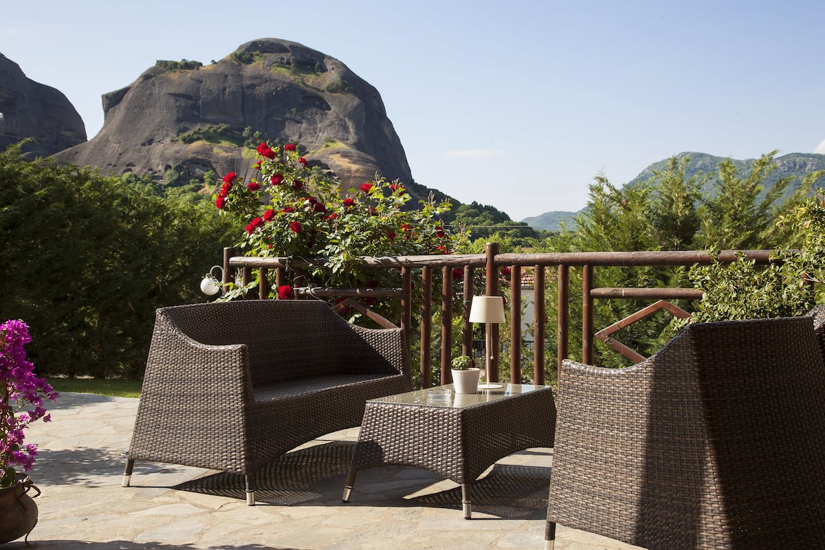 An outdoor seating area with wicker furniture and a table, surrounded by greenery and a mountainous backdrop.