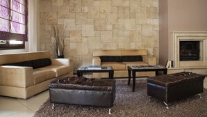 A living room with a beige sofa, a brown leather ottoman, a coffee table, and a fireplace. - Meteoritis Hotel (Kalabaka)