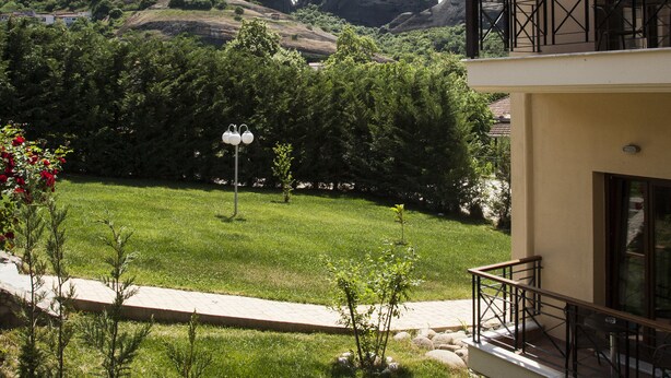 A hotel with a balcony overlooking a lush garden and a mountainous landscape. - Meteoritis Hotel (Kalabaka)