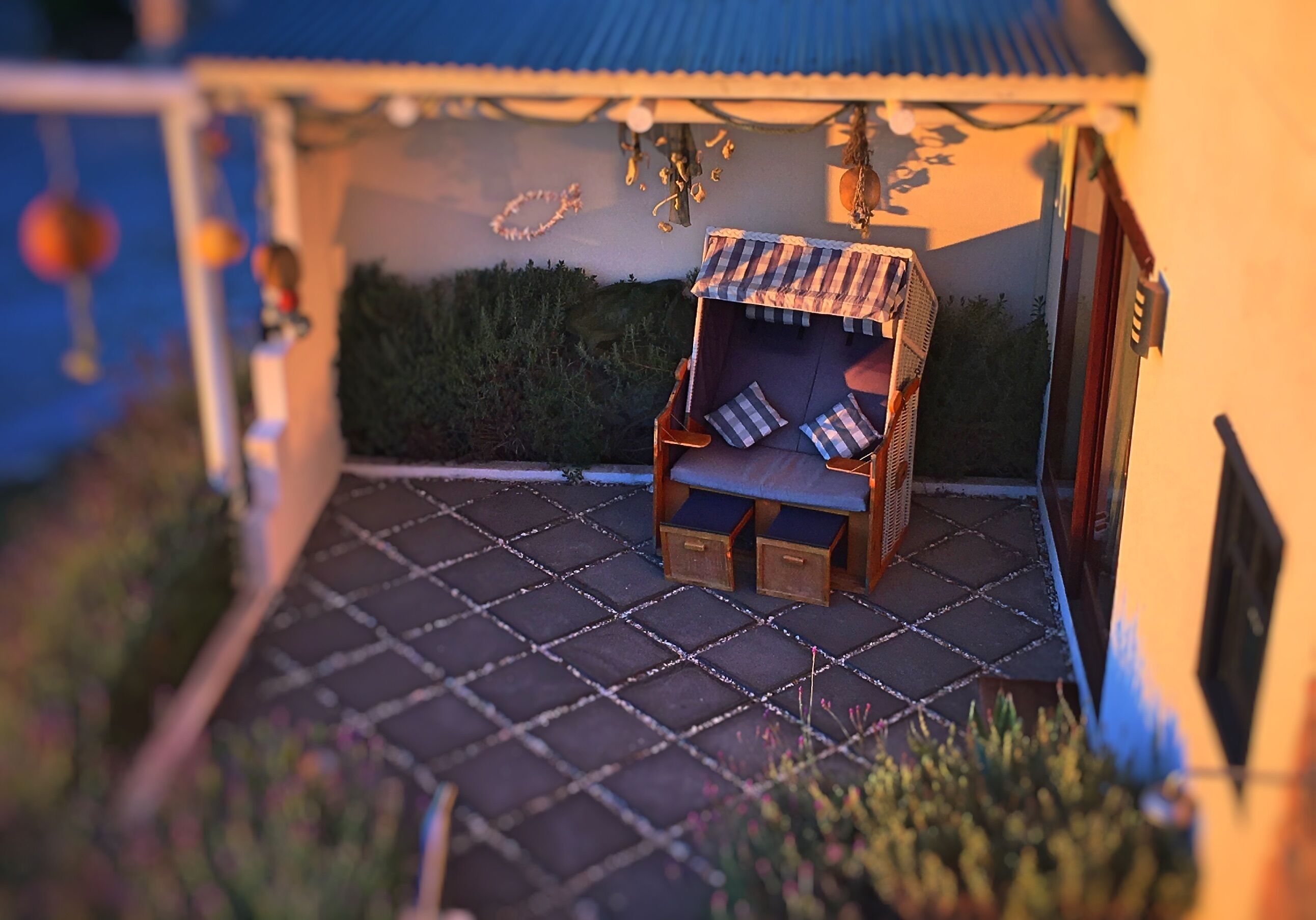 Un modelo de un espacio exterior acogedor con una silla colgante y una mesita, rodeado de un patio empedrado y una estructura con techo azul.
