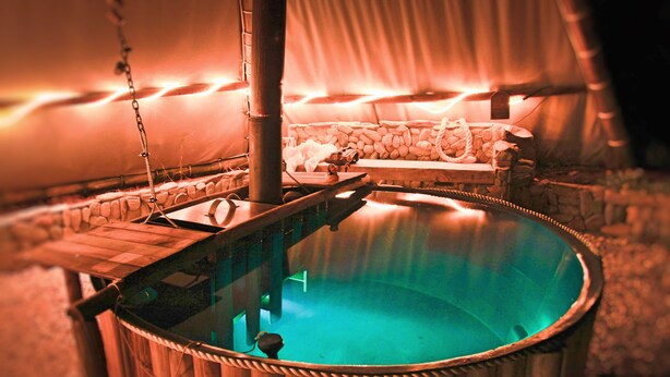 Un jacuzzi con estructura de madera y una pared de piedra al fondo.
