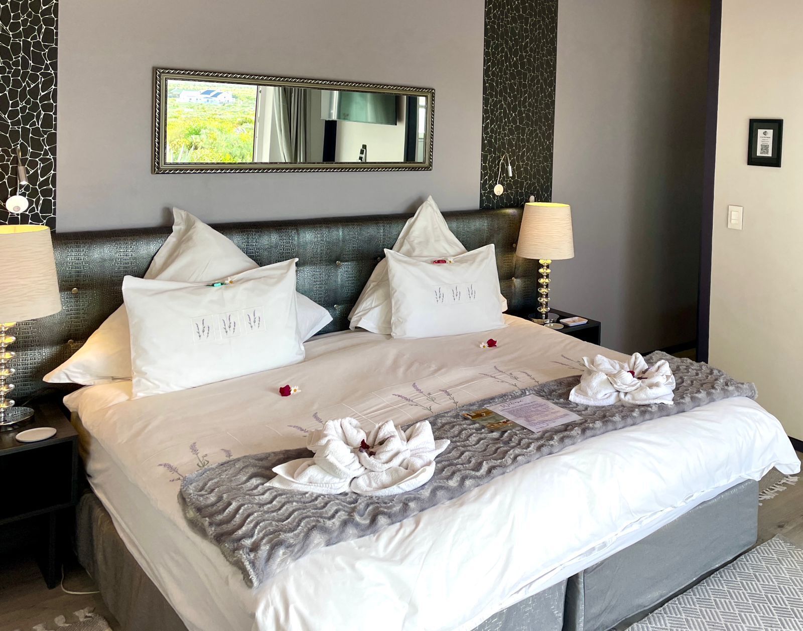 Una cama bien hecha con sábanas blancas, dos almohadas y una original disposición de toallas.