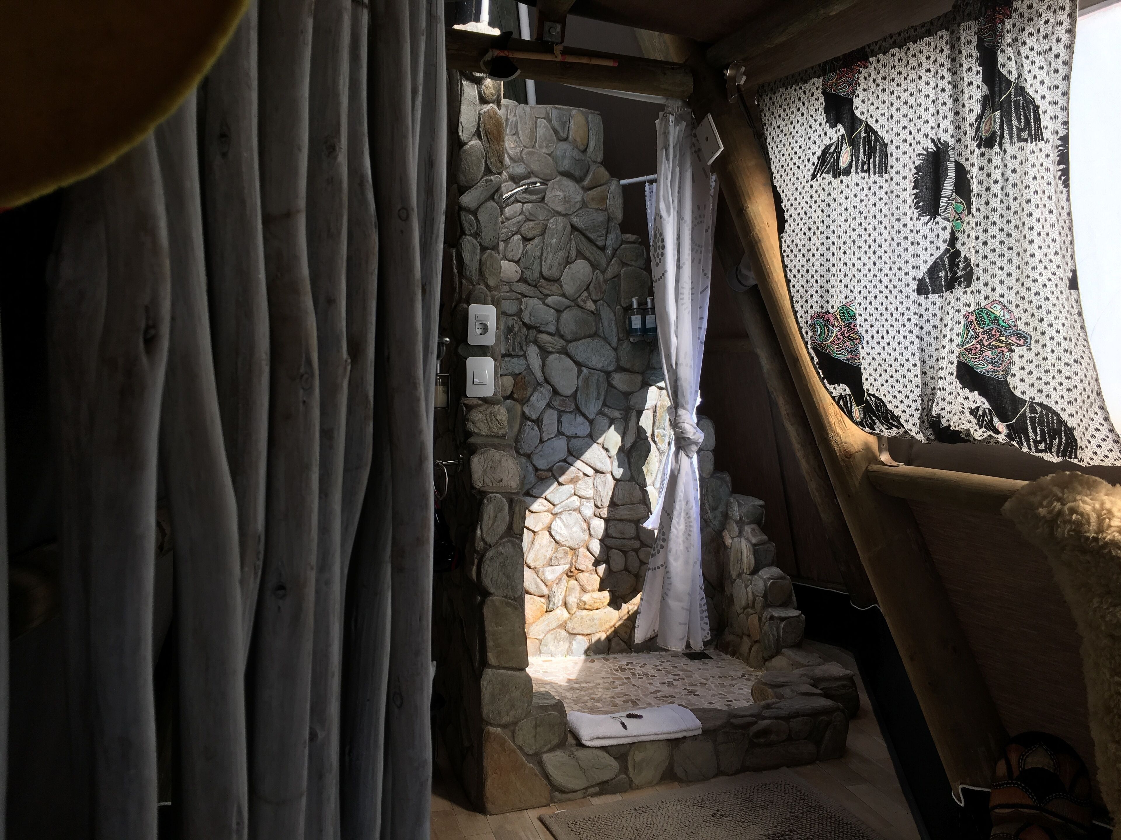 A stone-walled shower area with a white curtain, wooden beams, and a patterned wall.