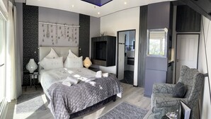 Un dormitorio moderno con una cama grande, un televisor y un rincón de descanso con una silla.