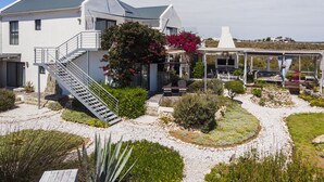 Una casa moderna con un área exterior cubierta, una escalera y un jardín con diversas plantas y flores.