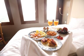 A neatly made breakfast table with plates of food and two glasses of orange juice on a bed in a hotel room.