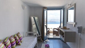 A bedroom with a bed, pillows, a bedside table, a mirror, and a view of the sea through an open door. - Caldera Romantica (Santorini)