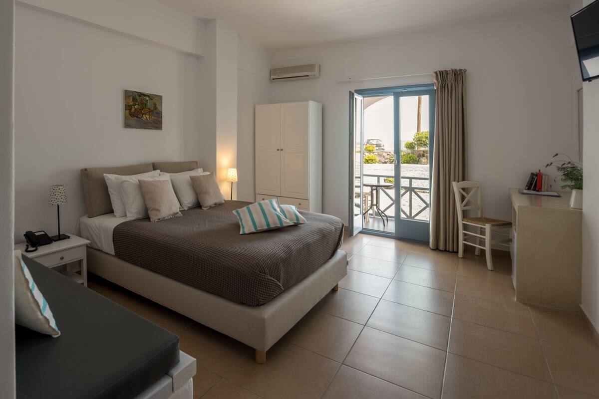 A modern bedroom with a large bed, a wardrobe, a desk, and a balcony with a view.