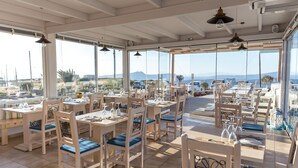 A restaurant with white tables and chairs, large windows, and a view of the landscape. - Caldera Romantica (Santorini)