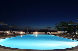 A swimming pool at night with lounge chairs and umbrellas. - Caldera Romantica (Santorini)