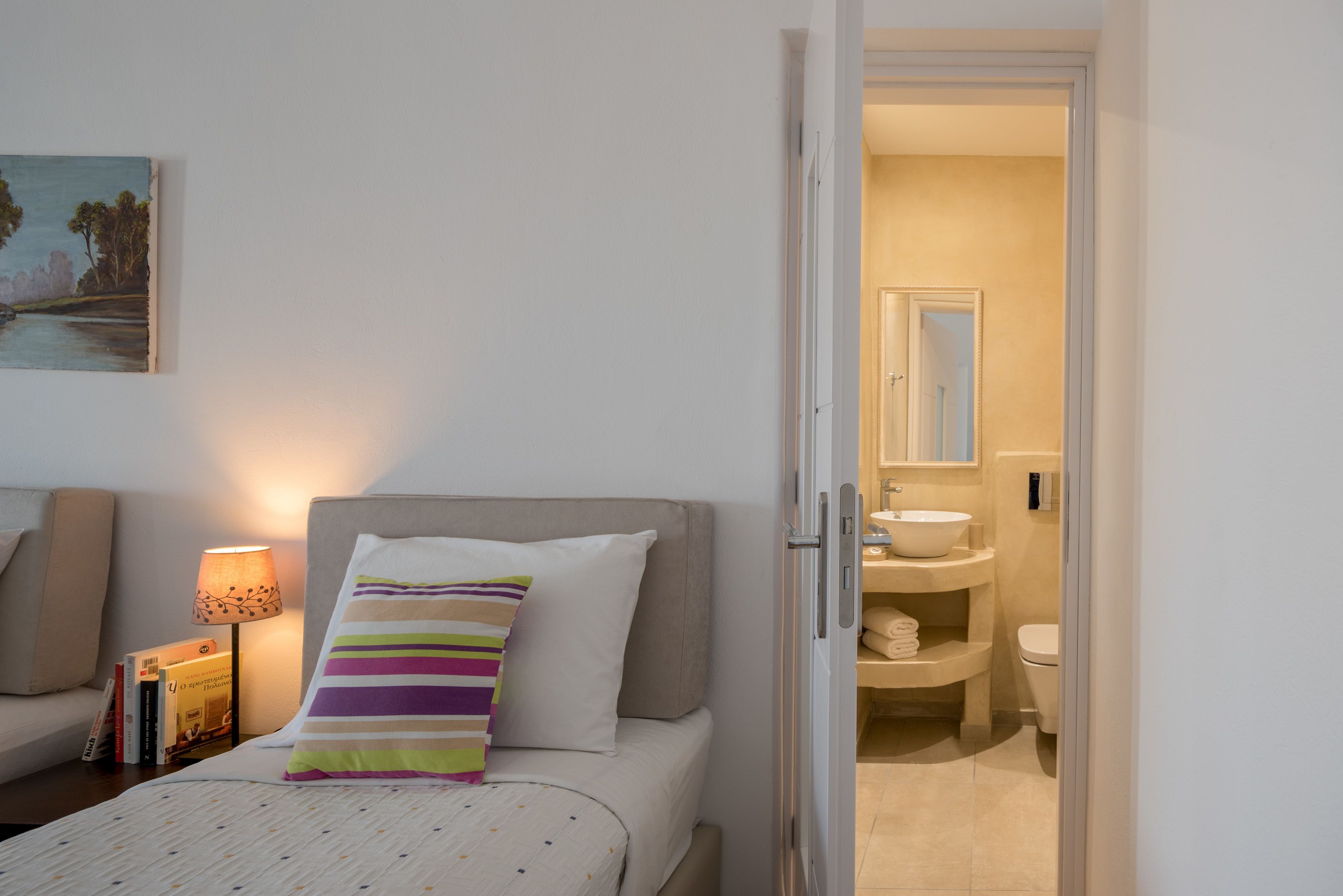 A hotel room with a bed, a bedside table with a lamp, a striped pillow, and a painting on the wall.