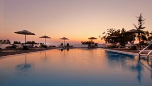 A swimming pool with lounge chairs and umbrellas, overlooking a sunset. - Caldera Romantica (Santorini)