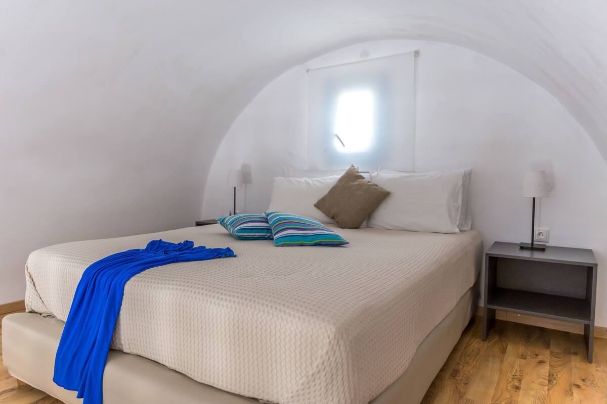 A bedroom with a large bed, a blue throw blanket, and a nightstand with a lamp.