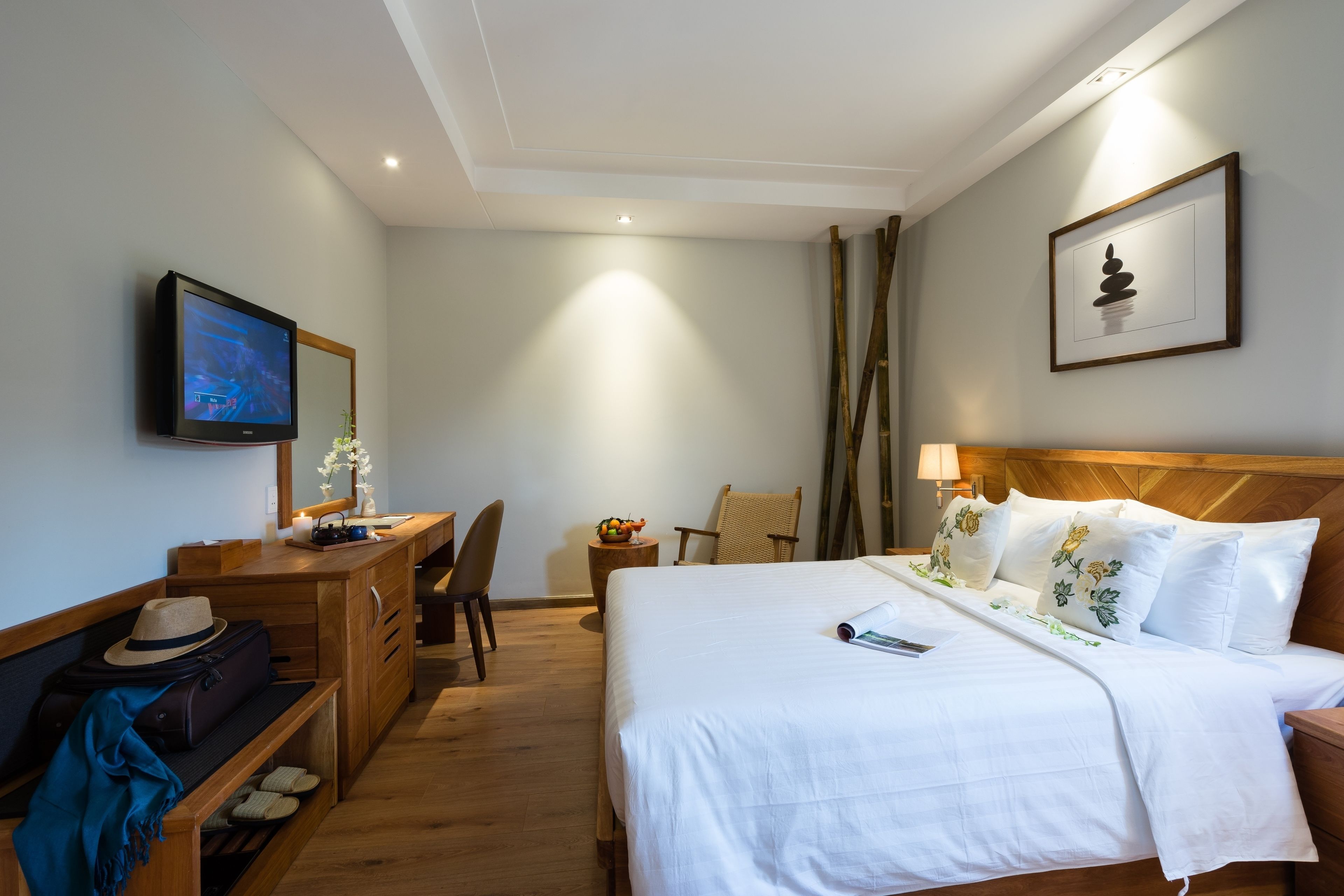 Habitación de hotel con cama, mesita de noche, televisor, escritorio, silla y una pequeña mesa con fruta.