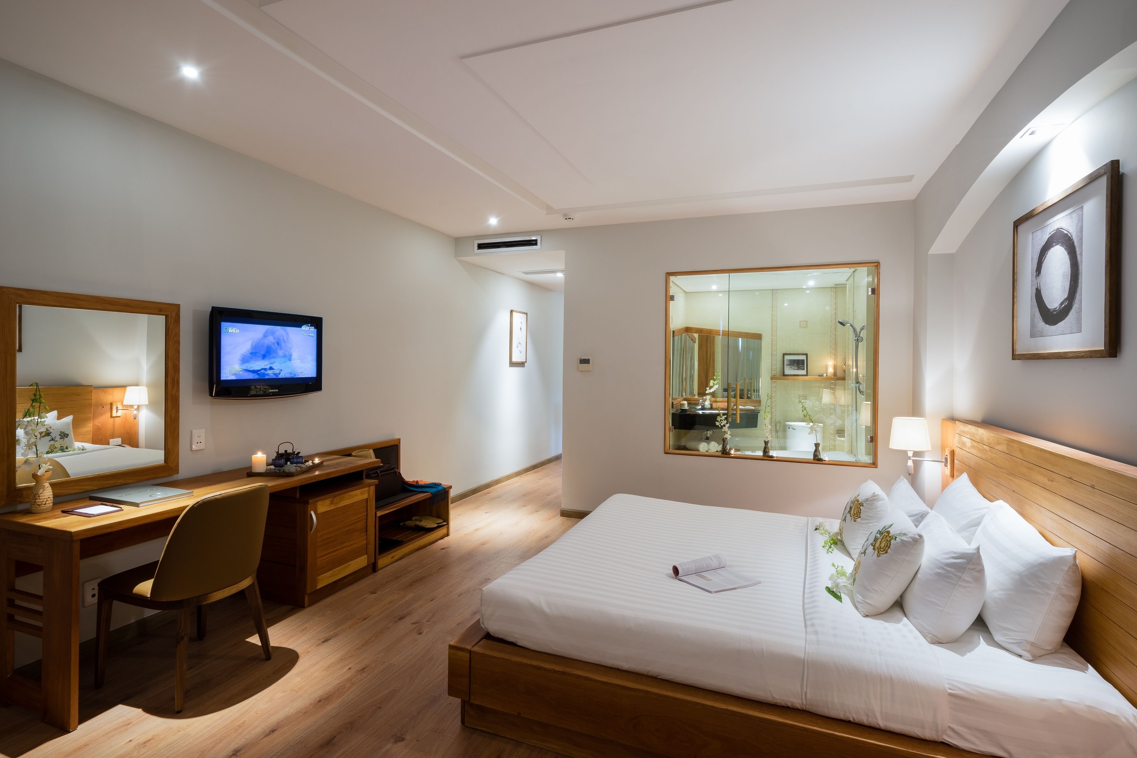 A hotel room with a wooden bed, a desk with a chair, a television, and a large mirror.