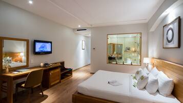 A hotel room with a wooden bed, a desk with a chair, a television, and a large mirror.
