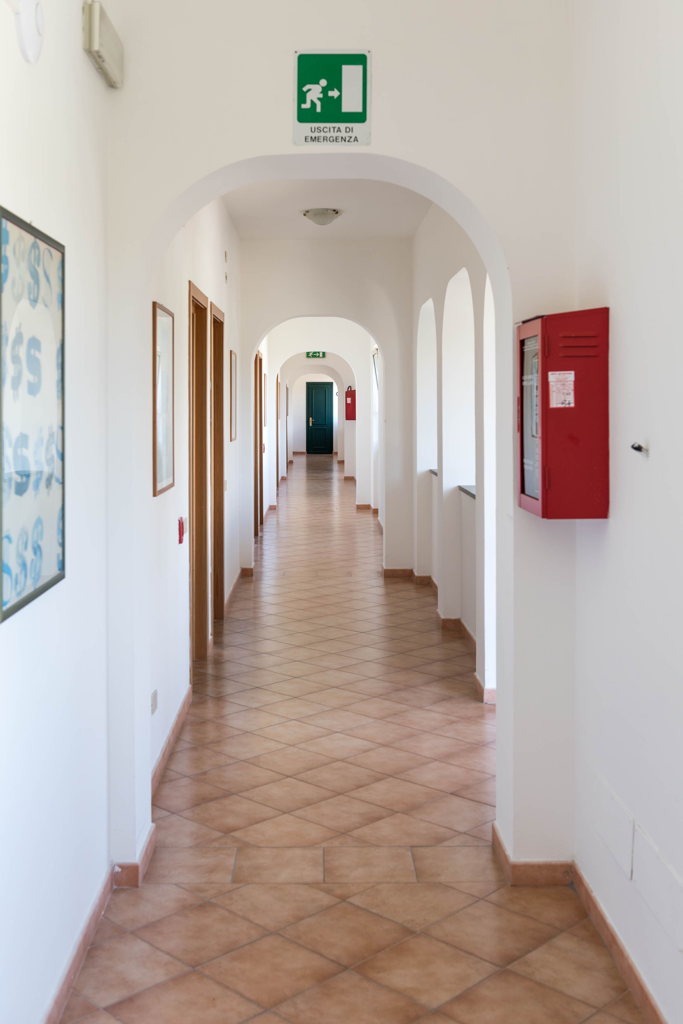 Ein Korridor mit gerahmten Kunstwerken an den Wänden, einem roten Notfallkasten und einem grünen Notausgangsschild.