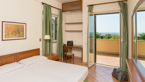 A hotel room with a bed, desk, chair, and a view of the sea. - Hotel Baia Del Sole (Civitavecchia)