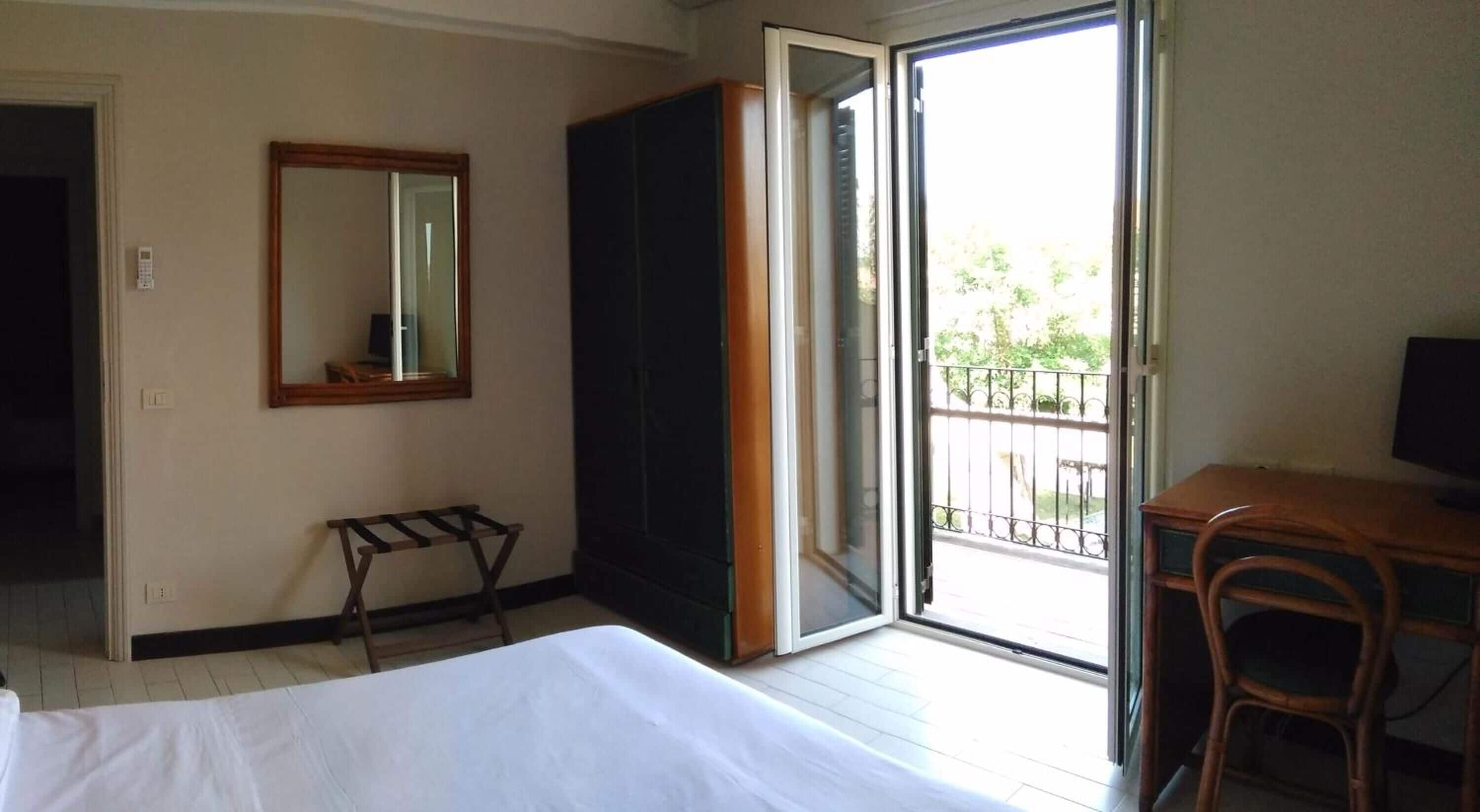 Une chambre d’hôtel comprenant un lit, un bureau, une chaise, un miroir et une porte-fenêtre coulissante donnant sur un balcon extérieur.