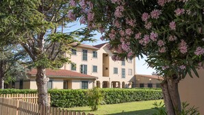 A two-story building with a red-tiled roof, surrounded by a wooden fence and lush greenery. - Hotel Baia Del Sole (Civitavecchia)