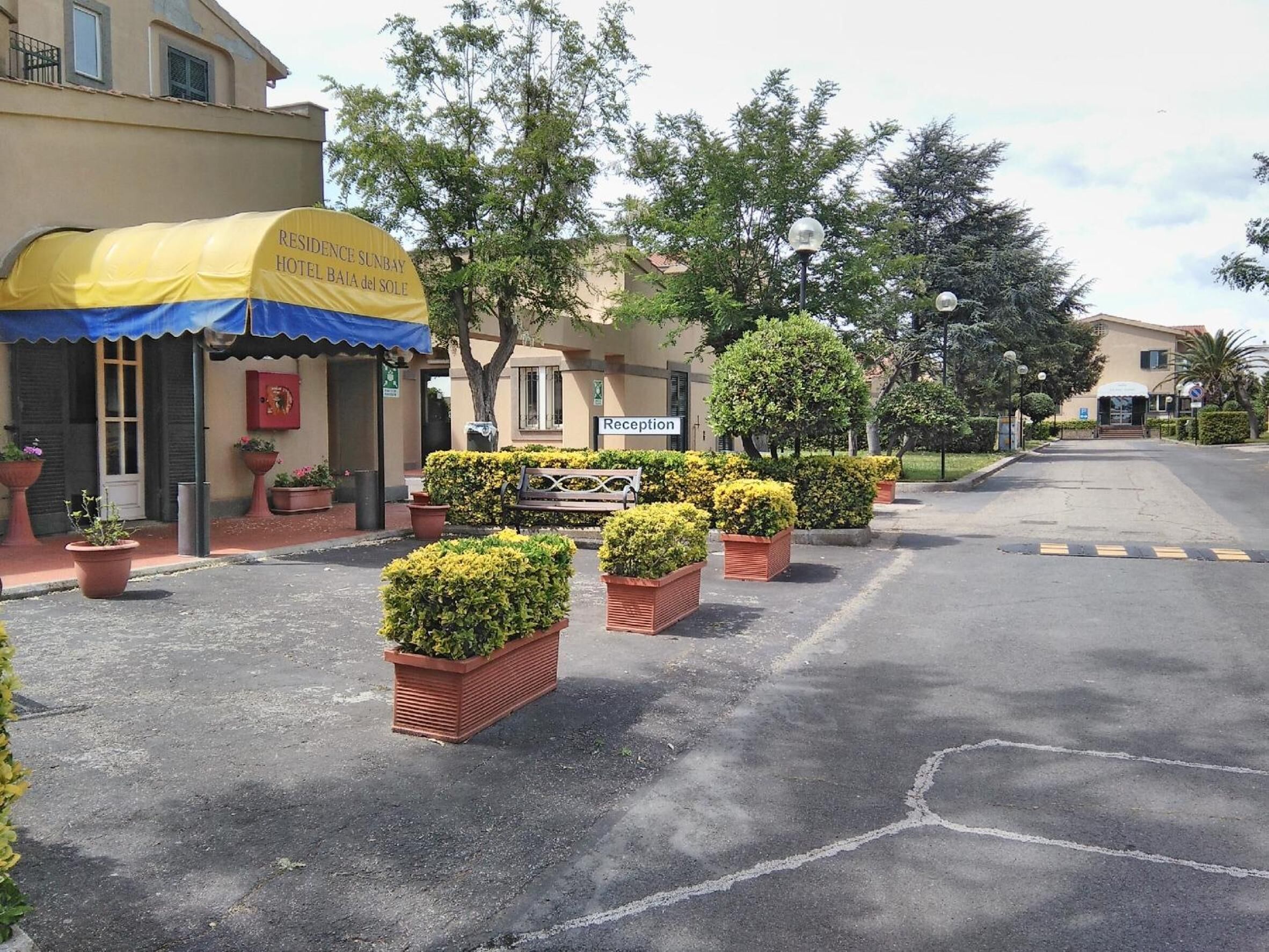 Ein Hotel mit Eingangsbereich, einer Rezeption, einem gelben Vordach und Blumentöpfen.