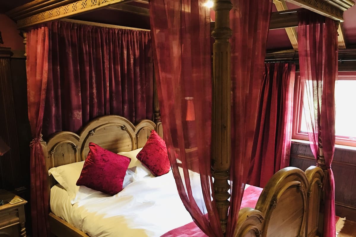 Un lit à baldaquin à quatre poteaux, avec des rideaux rouges, une tête de lit en bois et deux coussins rouges.