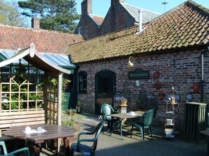 A brick building with a tiled roof, a sign reading 'Restaurant & Bar,' outdoor seating with tables and chairs, and a garden area with plants. - Wolds Village (Driffield)