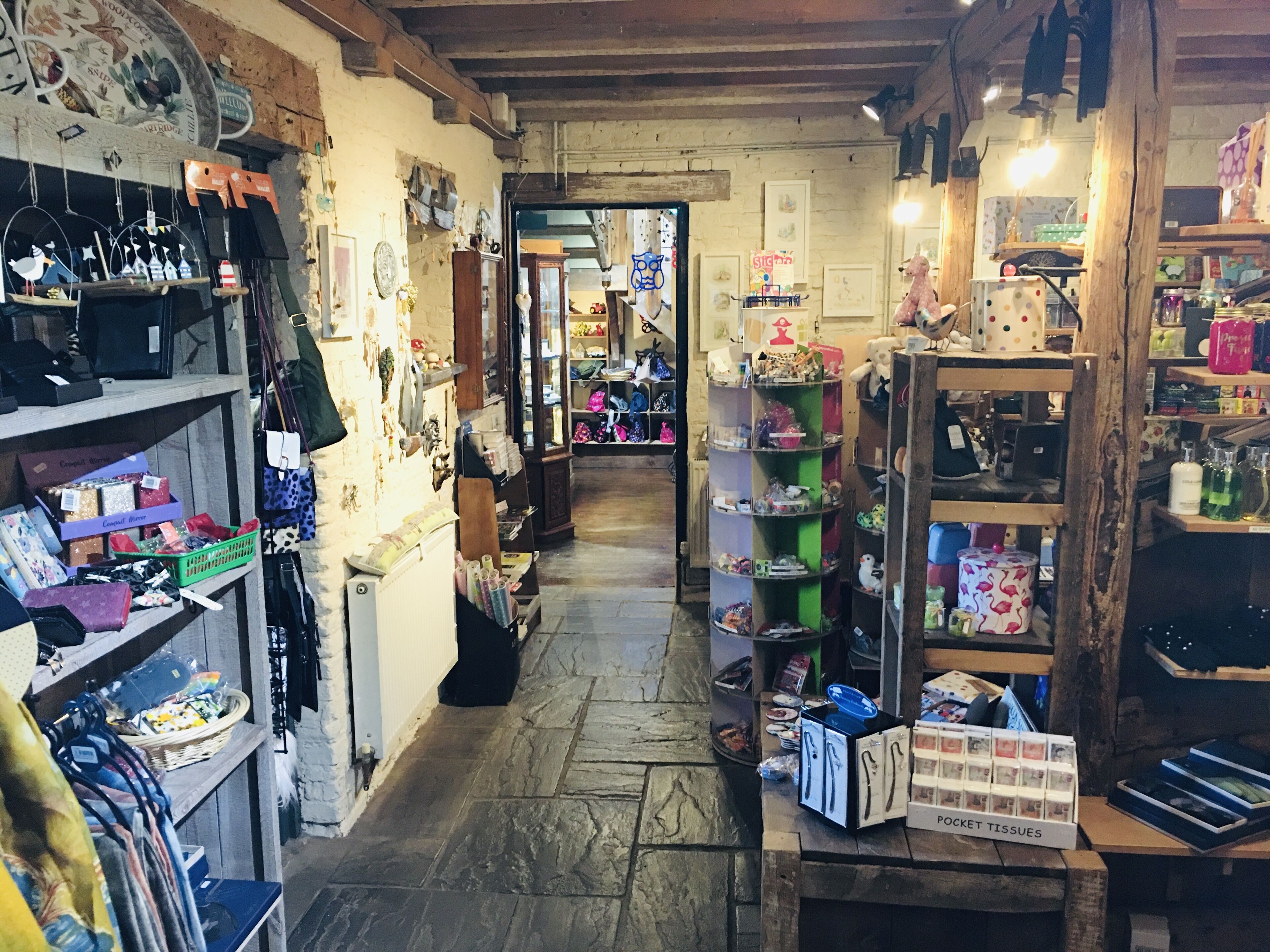A narrow, rustic shop with wooden shelves and displays of various items including handbags, jewelry, and other accessories.