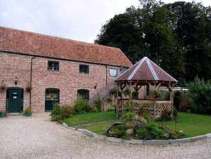 A brick building with a covered outdoor seating area, a gravel driveway, and a well-maintained garden. - Wolds Village (Driffield)