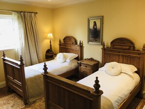 Una habitación con dos camas de madera, una mesita de noche con lámpara, un cuadro en la pared y una ventana con cortinas.