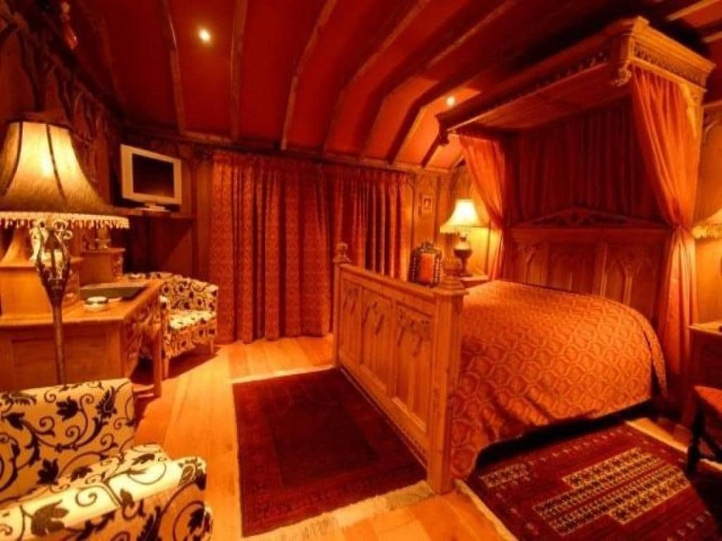 Een slaapkamer met een hemelbed, een televisie en een bureau met een lamp.