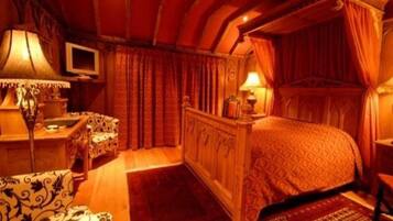 Een slaapkamer met een hemelbed, een televisie en een bureau met een lamp.
