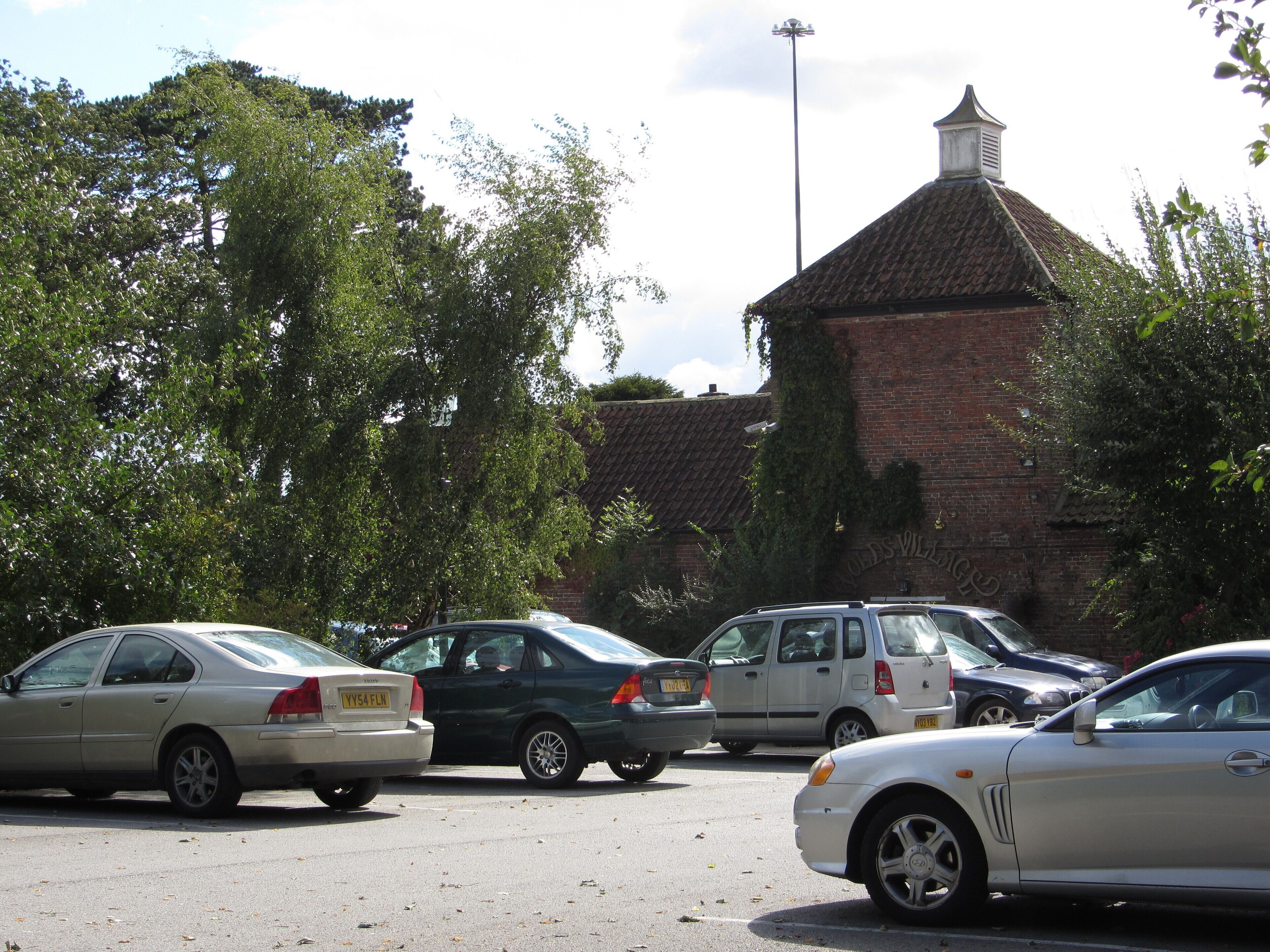 A parking lot with several cars, a brick building with a tower, and trees in the background.