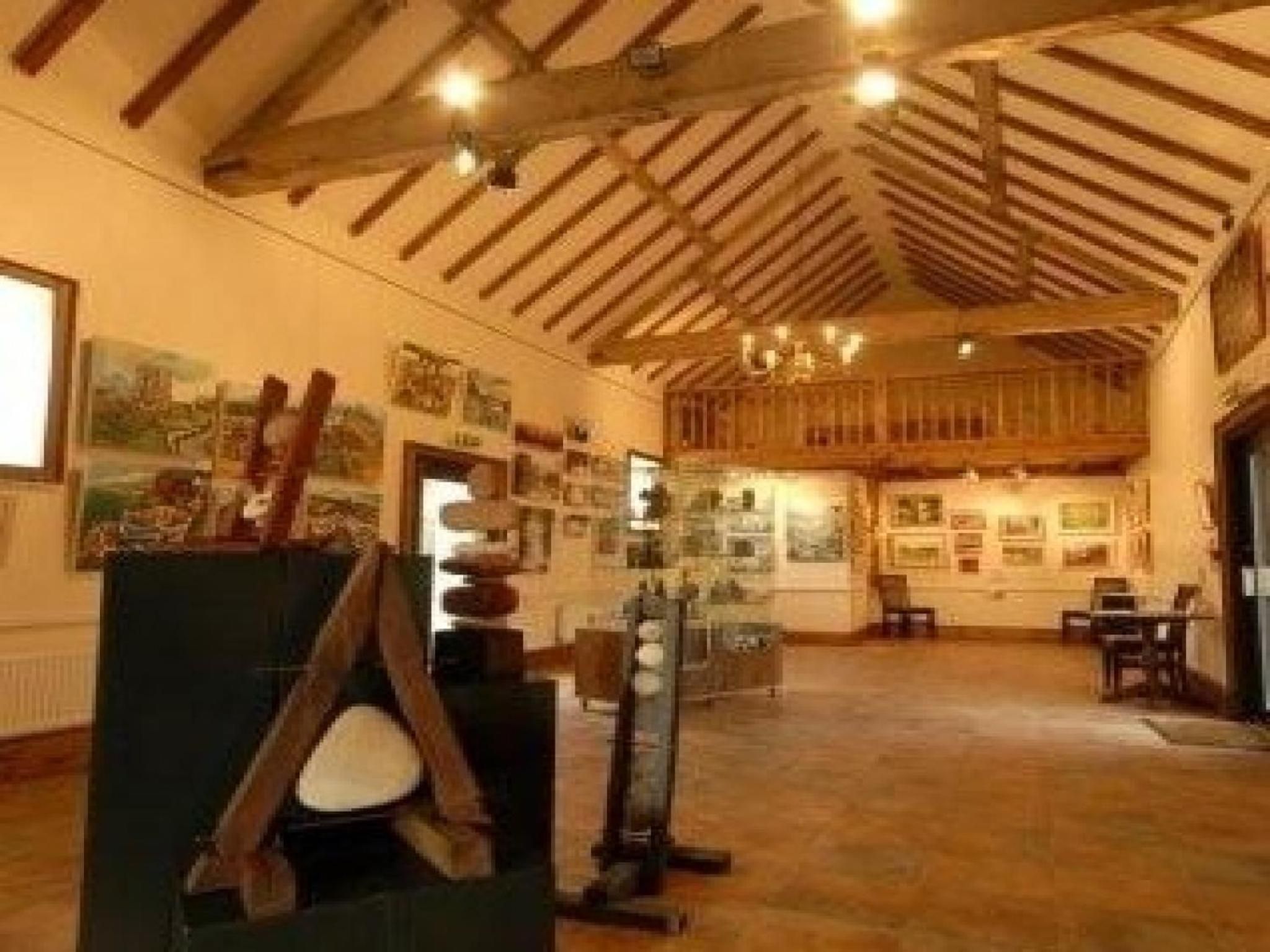 Una habitación amplia con vigas de madera en el techo, una chimenea y varias obras de arte en las paredes.