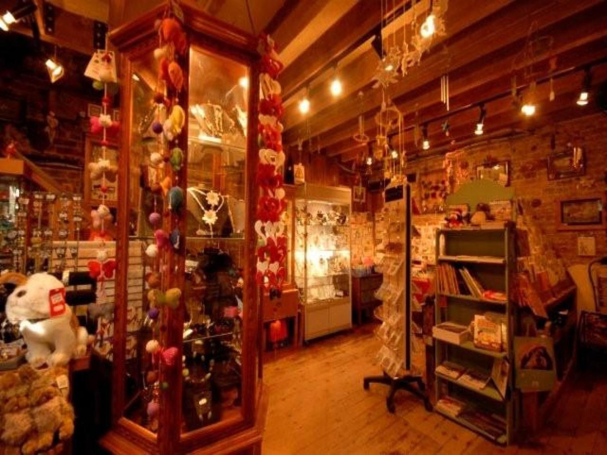 A cozy, warmly lit shop with wooden floors and walls, filled with various items like plush toys and jewelry displayed in glass cases.
