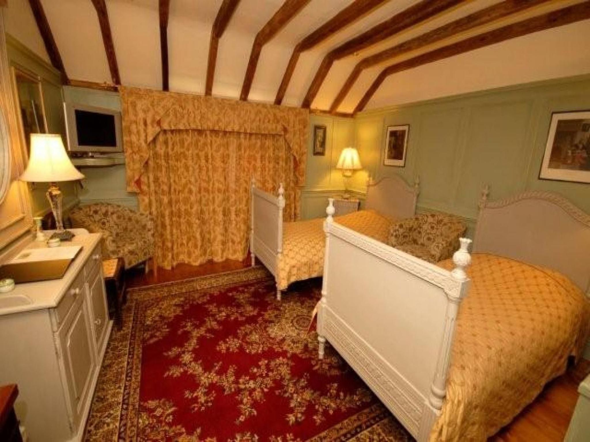 A room with a bed, bedside table, lamp, and a red patterned carpet.