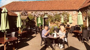 An outdoor patio with brick walls, green umbrellas, and outdoor seating. - Wolds Village (Driffield)