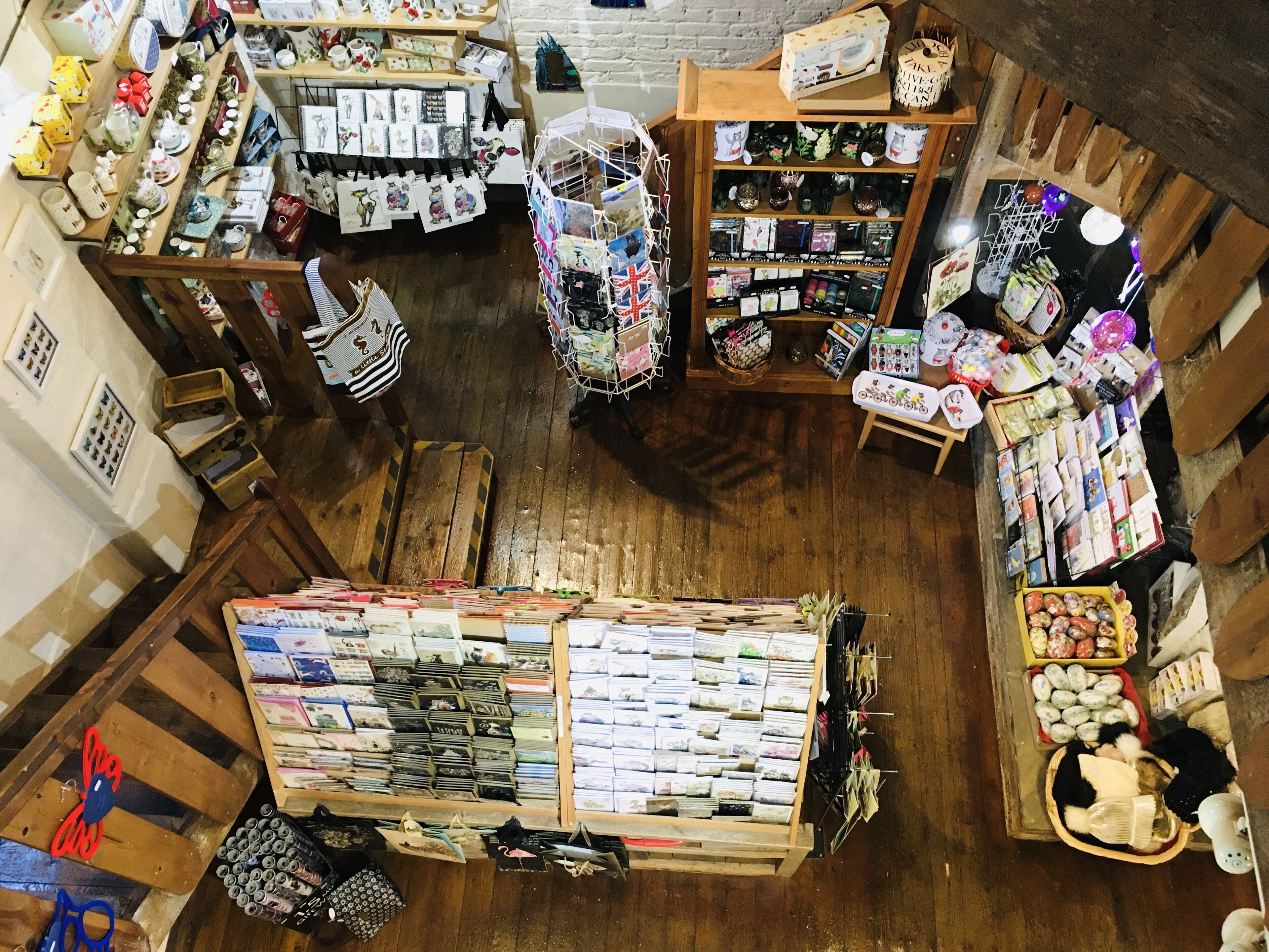 Uma livraria com diversos livros e revistas nas prateleiras, uma exposição de cartões de felicitações e uma seção com itens decorativos.