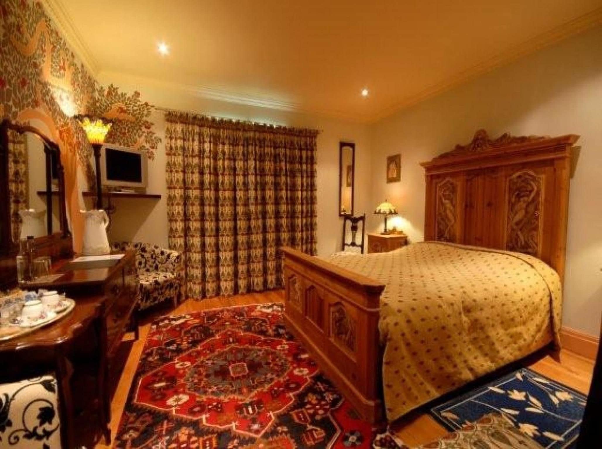 Ein traditionell eingerichtetes Zimmer mit einem Bett, einem Schreibtisch, einem Sessel, einem Fernseher und einem gemusterten Teppich.