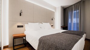 Une chambre d’hôtel avec un grand lit, des tables de chevet, des lampes fixées au mur et une vue sur l’extérieur.
