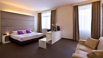 Une chambre d’hôtel moderne équipée d’un lit, d’un bureau, d’un canapé et de grandes fenêtres avec des rideaux.